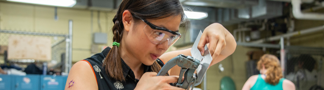 Person wearing safety glasses using a tool to punch a hole in metal