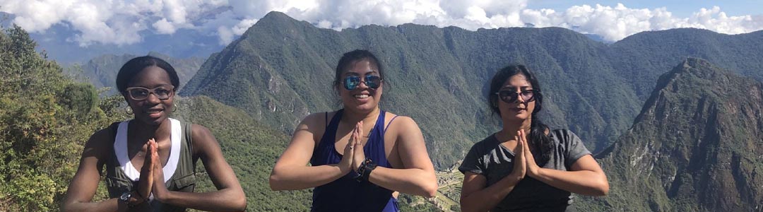 3 women stand outside with mountains in background