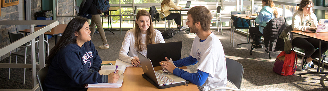 Three students, one male, two female, sitting at a table in a study lounge