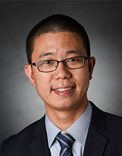 headshot of a man wearing glasses, a light blue shirt, suit jacket and tie