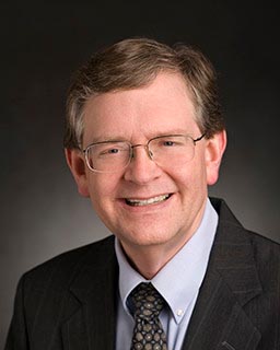 head shot of a man with glasses wearing a suit and tie