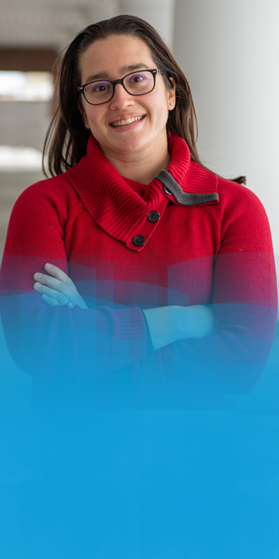 An individual wearing a red sweater with arms crossed poses outdoors