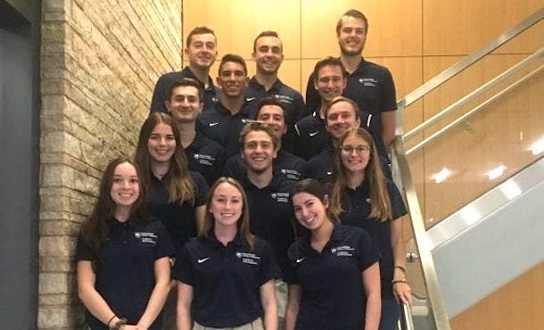 A group of students in blue Penn State polo shirts posing on steps