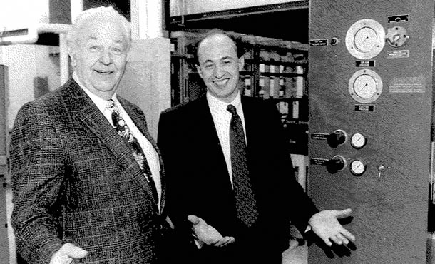 two men standing and smiling in front of lab equipment