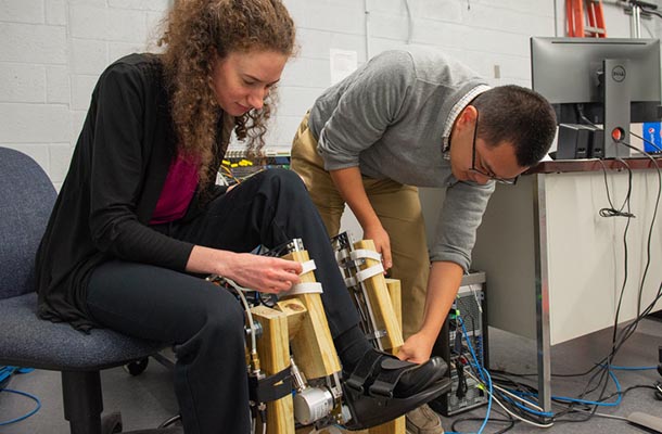 a caucasian woman and an asian man work with a robotic exoskeleton