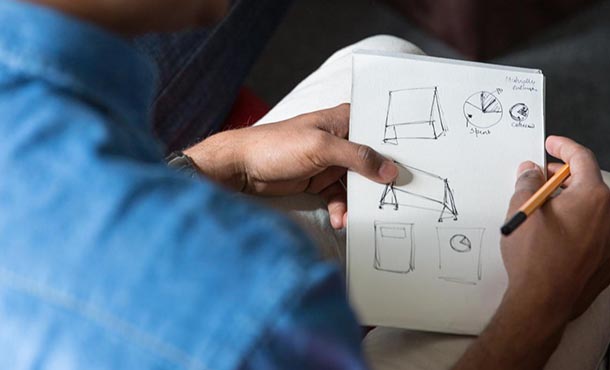 A man holds a piece of paper with rough design sketches on it.