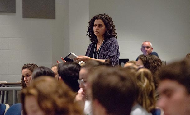 A woman stands to speak, surrounded by other students in an auditorium.