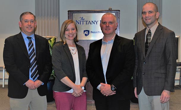 Three men and one woman stand and smile in front of a podium.