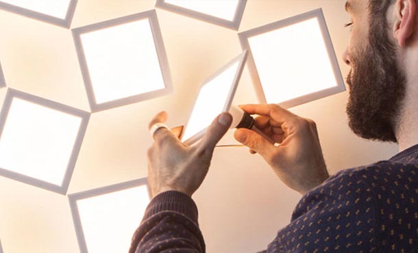 A man holds an organic LED luminaires in front of a wall that contains several more identical luminaires