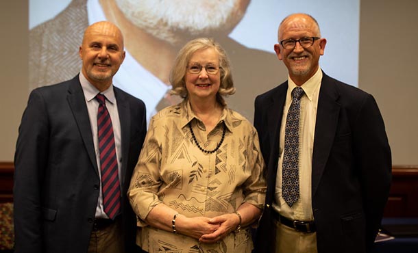 A woman stands between two men, all three of whom are smiling and facing the camera.