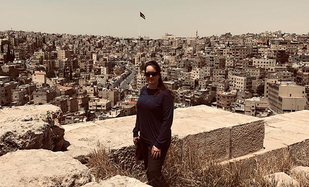 A woman wearing dark clothing stands at an overlook of a city with hundreds of buildings behind her.