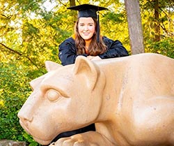 woman wearing cap and gown poses at the nittany lion shrine