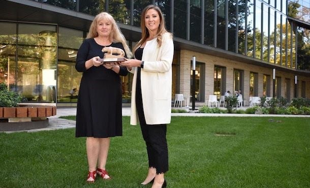 two women outside of a building holding an award