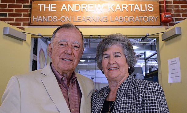 Andrew and Katherine Kartalis smile at the camera. The background, a sign reading The Andrew Kartalis Hands-On Learning Laboratory can be seen.
