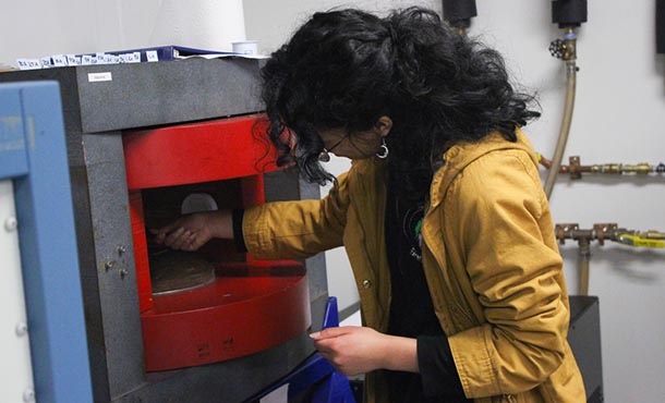 A female high school student works with a piece of machinery in a lab.