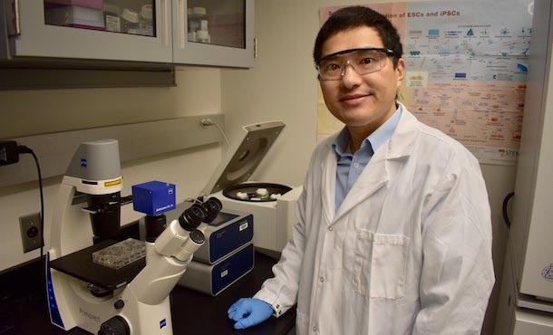 Man in lab coat standing next to a microscope