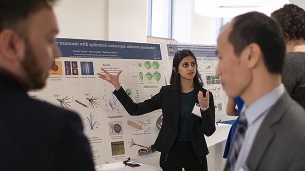 A woman speaking about the research displayed on a large poster to her left.