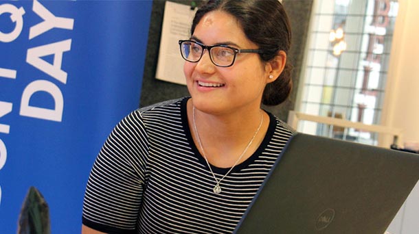 Hispanic female sitting behind the screen of a laptop computer smiling