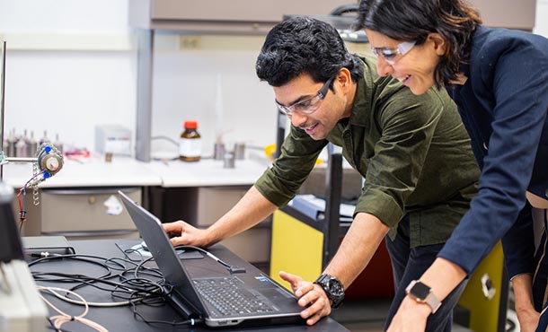 a man and woman look at a lap top computer screen