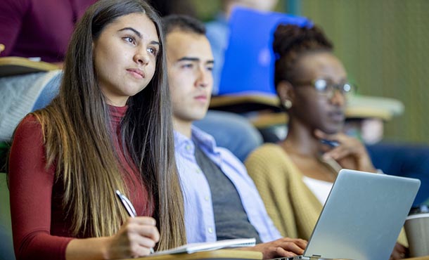 students sit in a lecture style hall while taking class notes