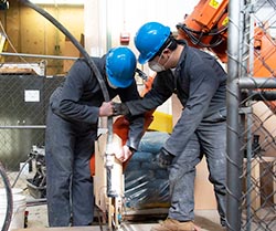 Two students hold on to a black tube attached to a piece of wood