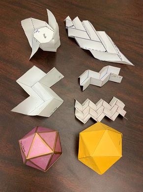 Seven origami paper structures are displayed on a brown table. Each structure is different.