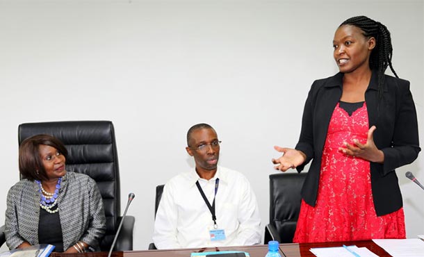 woman standing next to a man and woman, who are seated at a table.