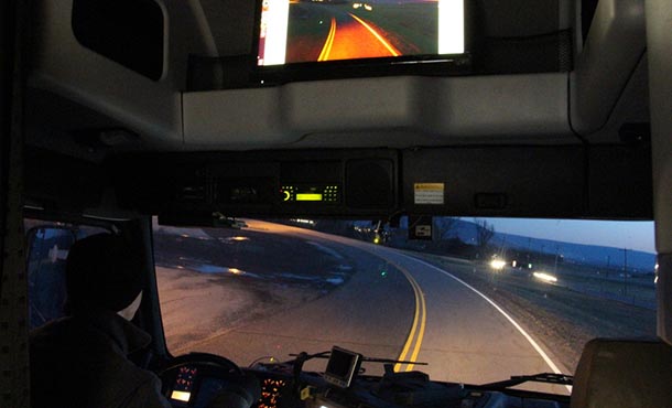 View of a marked roadway from inside a truck cabin with computer screens showing an image of the same road.