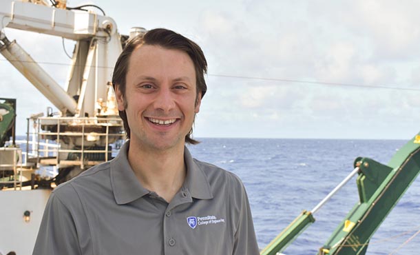 A man in a polo shirt stands on a boat in front of the ocean.