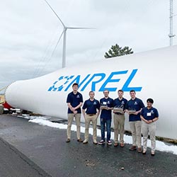 Six students pose with trophies next to a wind turbine blade