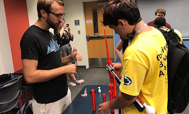 two men look at red, 3D-printed cylinder pieces