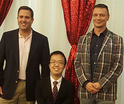 A man of short stature stands with two men, all wearing suits. 