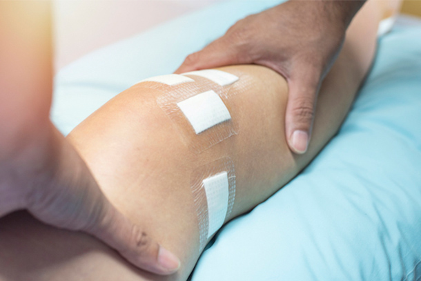  A doctor's hands on a patient's leg while checking knee on exam table.