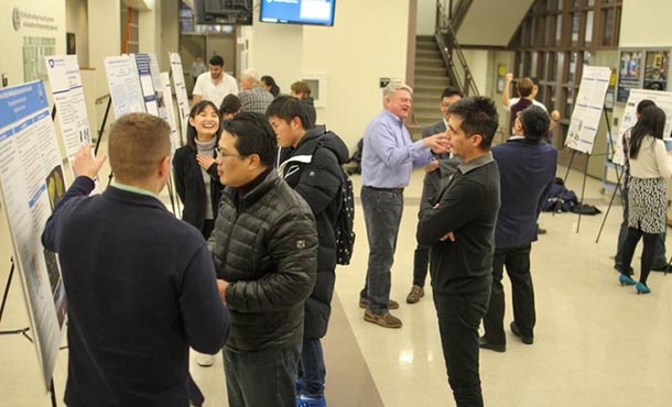 A group gathers in a large lobby area to view and discuss research posters