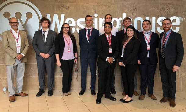 Ten people in business clothes stand in front of a silver sign that reads Westinghouse. They are all posed, looking at the camera.