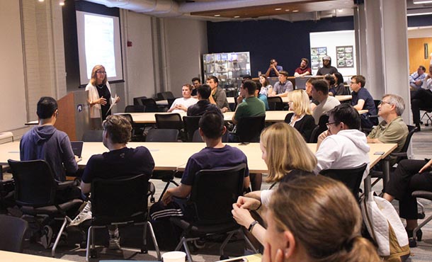 A woman delivers a lecture in front of students, faculty and staff.