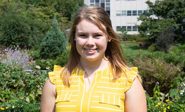 A blonde undergraduate female student smiles in a garden.