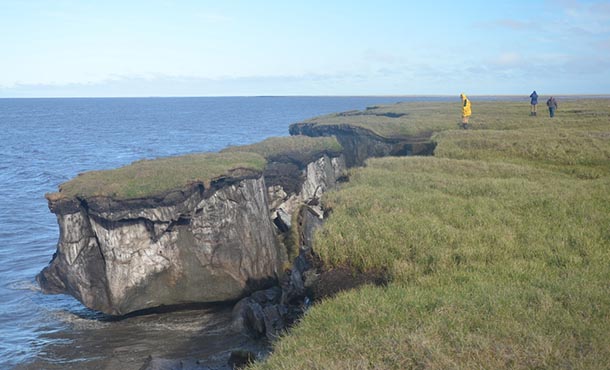 A large chunk of grassy land splits away from the coast, falling into the ocean.